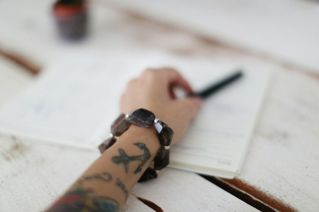 Hands writing research notes on paper at a wooden desk